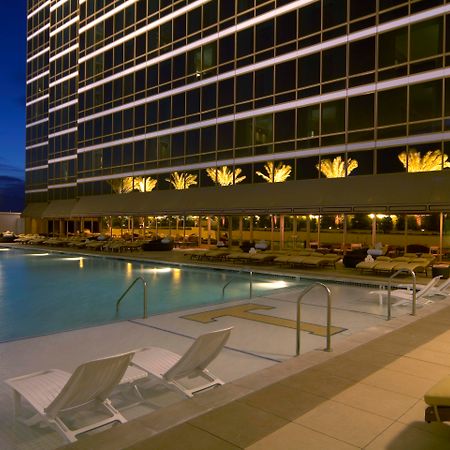 Trump International Hotel Лас Вегас Съоръжения снимка The photo depicts a modern and elegant outdoor swimming pool area in the evening. The pool is surrounded by lounges and chairs, creating a relaxing atmosphere. In the background, there is a tall, contemporary building with large windows, which are il