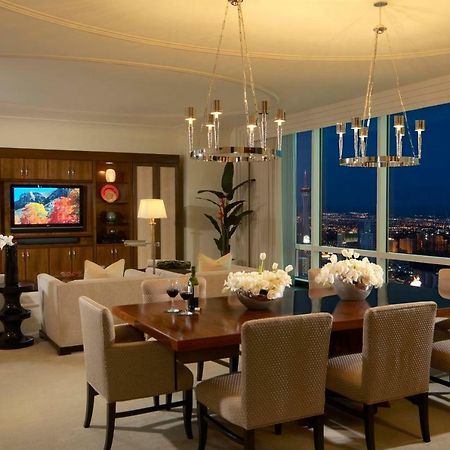 Trump International Hotel Лас Вегас Стая снимка The photo shows an elegantly designed living and dining area. The space features a large oval dining table surrounded by upholstered chairs. A decorative centerpiece with flowers adorns the table. On one side, there's a cozy seating arrangement with 