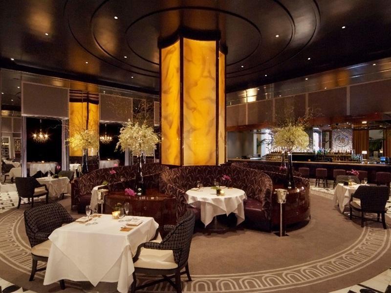 Trump International Hotel Лас Вегас Екстериор снимка The photo depicts an elegant restaurant interior featuring a luxurious ambiance. There are round tables set with white tablecloths, each with tasteful decor. The seating includes plush, dark leather booths and elegant wicker chairs. 

A striking cent