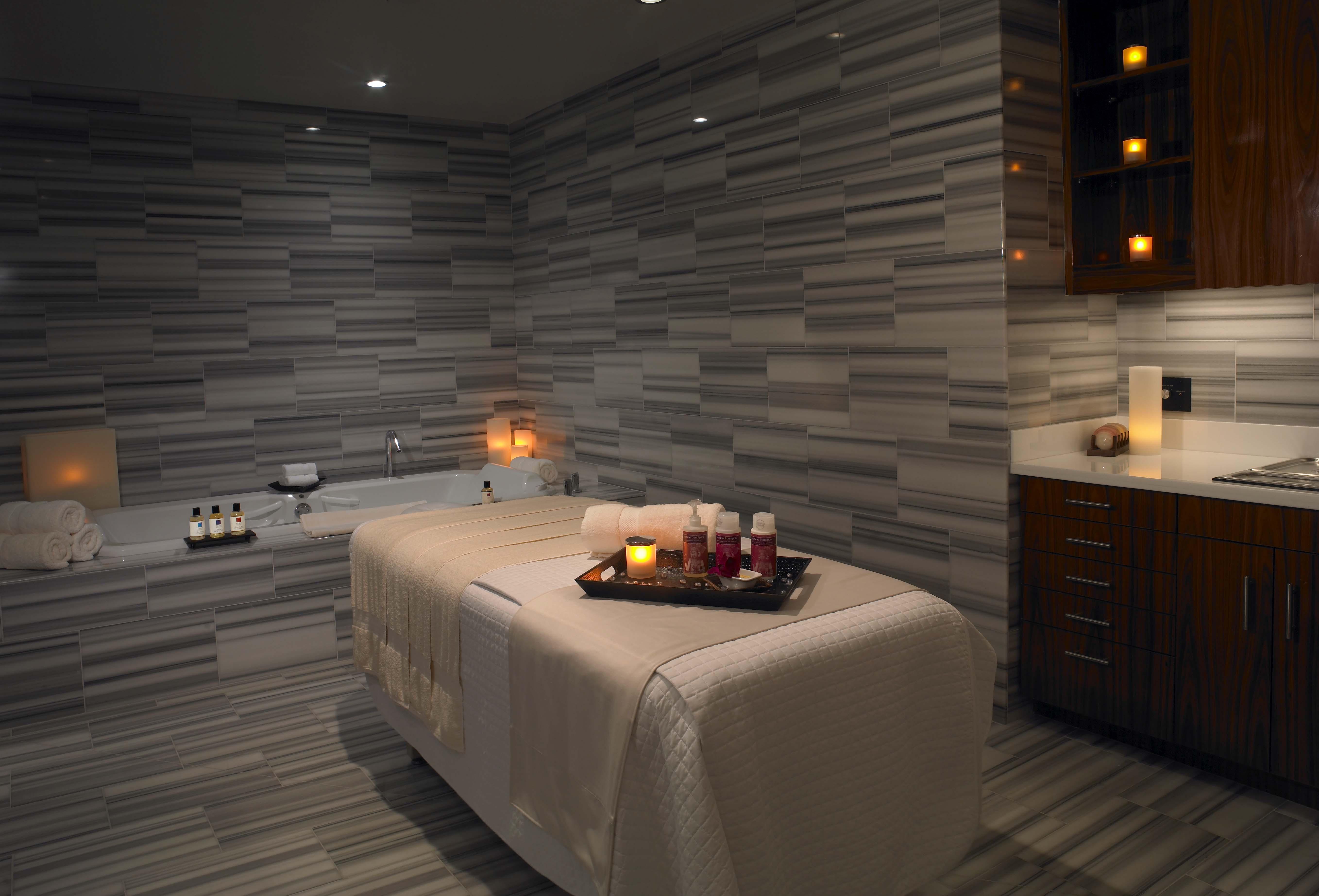 Trump International Hotel Лас Вегас Съоръжения снимка The photo shows a serene spa room designed for relaxation. There is a massage table covered with a soft white blanket at the center. Next to the table, a tray is arranged with several small cups or bottles, likely containing oils or beverages, and de