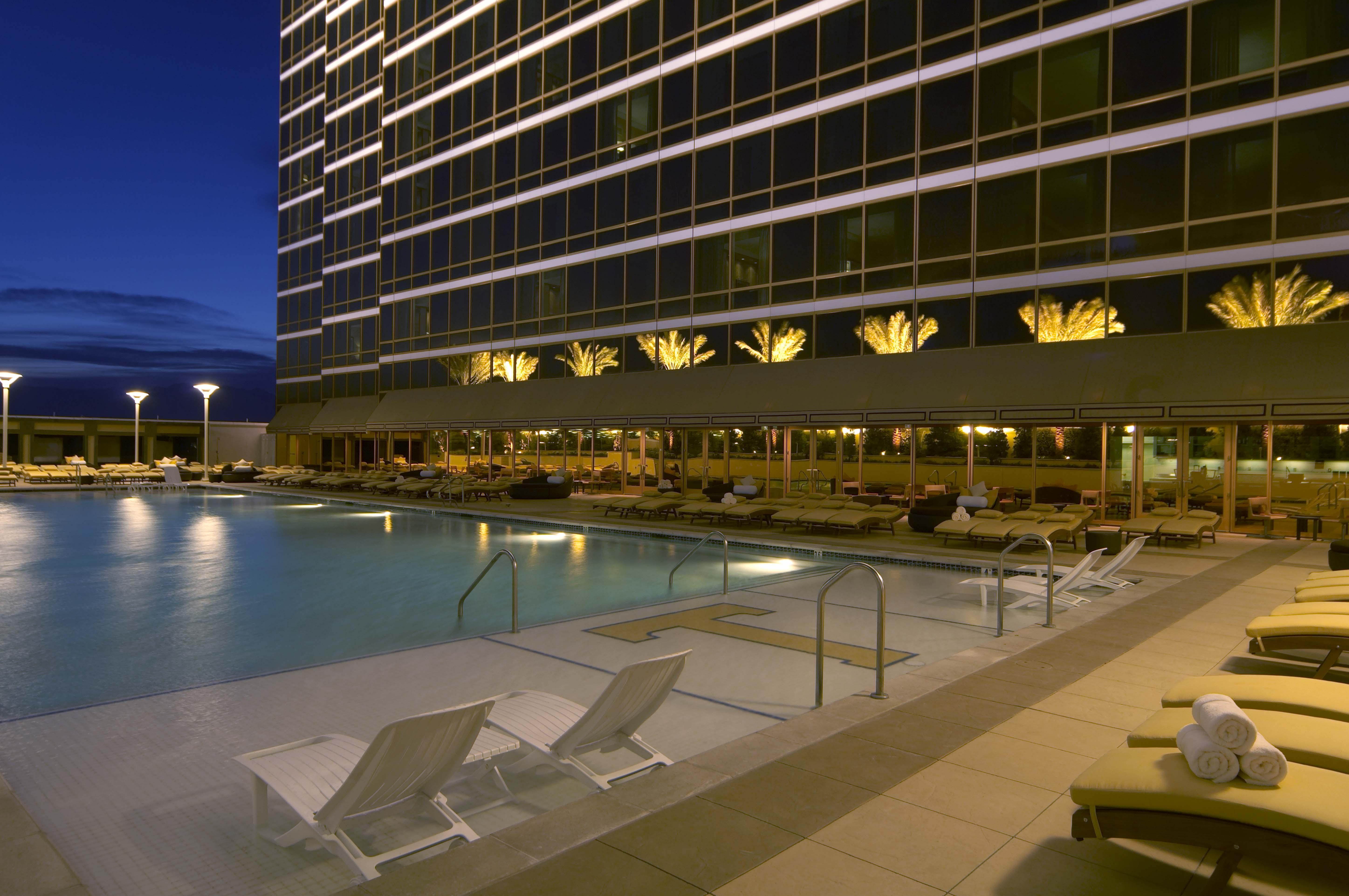 Trump International Hotel Лас Вегас Съоръжения снимка The photo depicts a modern and elegant outdoor swimming pool area in the evening. The pool is surrounded by lounges and chairs, creating a relaxing atmosphere. In the background, there is a tall, contemporary building with large windows, which are il