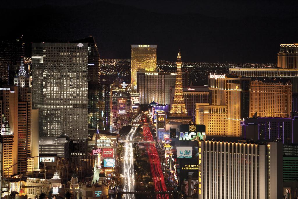 Trump International Hotel Лас Вегас Екстериор снимка The photo showcases a vibrant night view of the Las Vegas Strip, illuminated by numerous lights and neon signs. The scene features tall buildings, including hotels and casinos, with distinctive architectural designs. The iconic Eiffel Tower replica c
