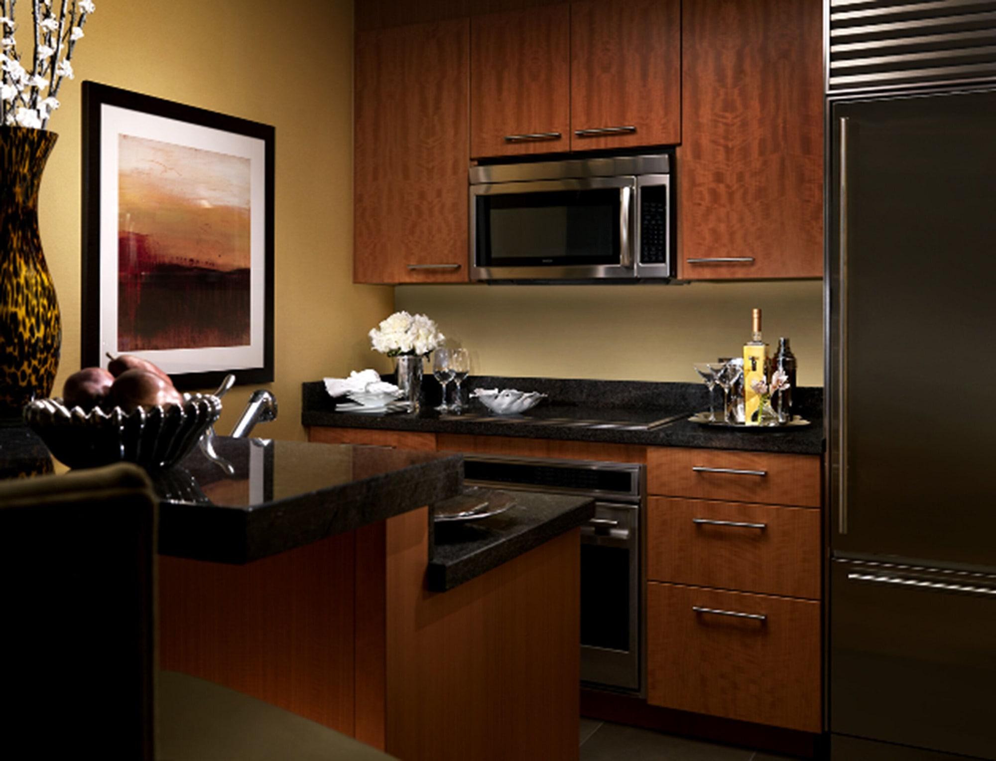 Trump International Hotel Лас Вегас Екстериор снимка The photo shows a modern kitchen with a warm and sleek design. It features wooden cabinets with a rich finish, a black countertop, and stainless steel appliances, including a microwave and refrigerator. There's a framed piece of abstract artwork on t
