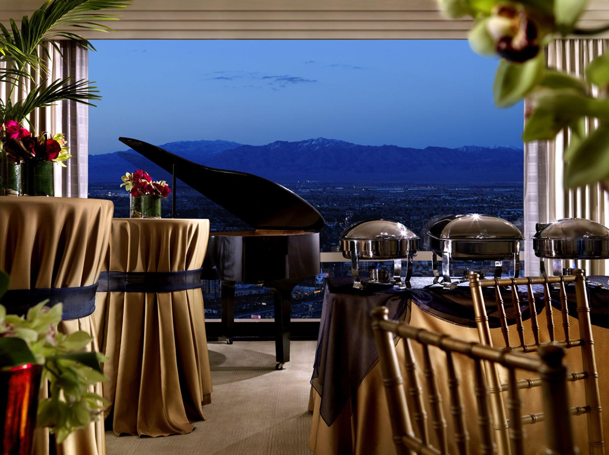 Trump International Hotel Лас Вегас Екстериор снимка The photo features an elegantly arranged event space with a grand piano positioned near a large window, showcasing a scenic view of mountains at dusk. There are tables with gold tablecloths, accented by dark blue ribbons, and decorative flower arrang