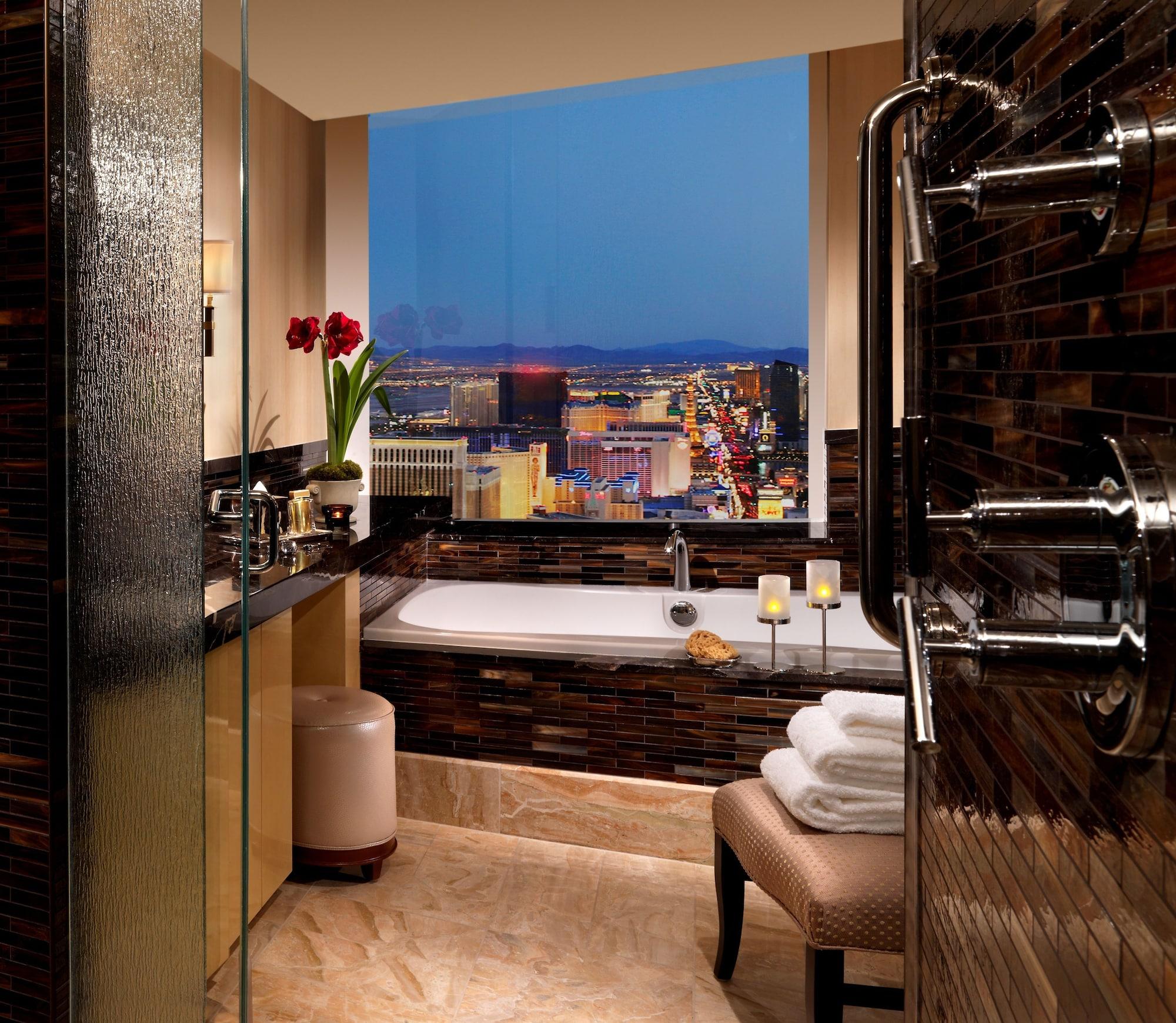 Trump International Hotel Лас Вегас Екстериор снимка The photo shows a luxurious bathroom with a modern design. The space features a large window with a stunning view of a city skyline at dusk, illuminated by city lights. Inside the bathroom, there's a stylish bathtub, a glass-enclosed shower with mult