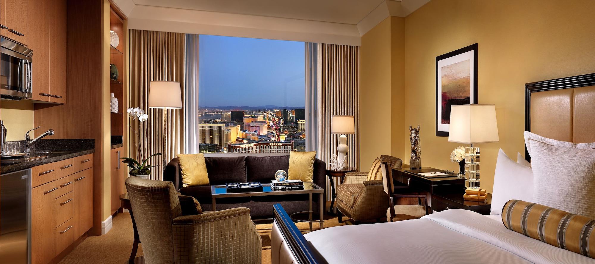 Trump International Hotel Лас Вегас Екстериор снимка The photo shows a stylish hotel room with contemporary decor. It features a large window that offers a view of a cityscape, likely at dusk, as the sky transitions to evening. Inside the room, there are two comfortable chairs and a small table, elegan