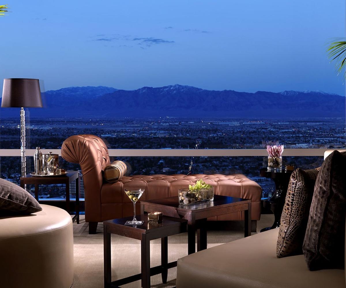 Trump International Hotel Лас Вегас Екстериор снимка The image depicts a stylish and luxurious lounge area with a stunning view of the mountains in the background at twilight. The furniture includes a modern brown leather chaise lounge, a round coffee table, and additional seating options. There are el