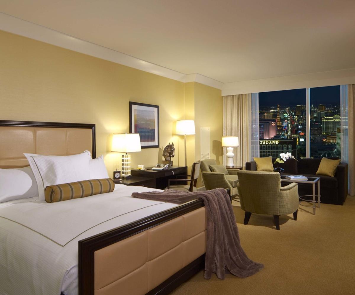 Trump International Hotel Лас Вегас Екстериор снимка The photo shows a luxurious hotel room. It features a large bed with a beige and white color scheme, complemented by a decorative pillow and a plush throw blanket. The room has an elegant atmosphere with warm yellow walls and soft lighting from bedsi