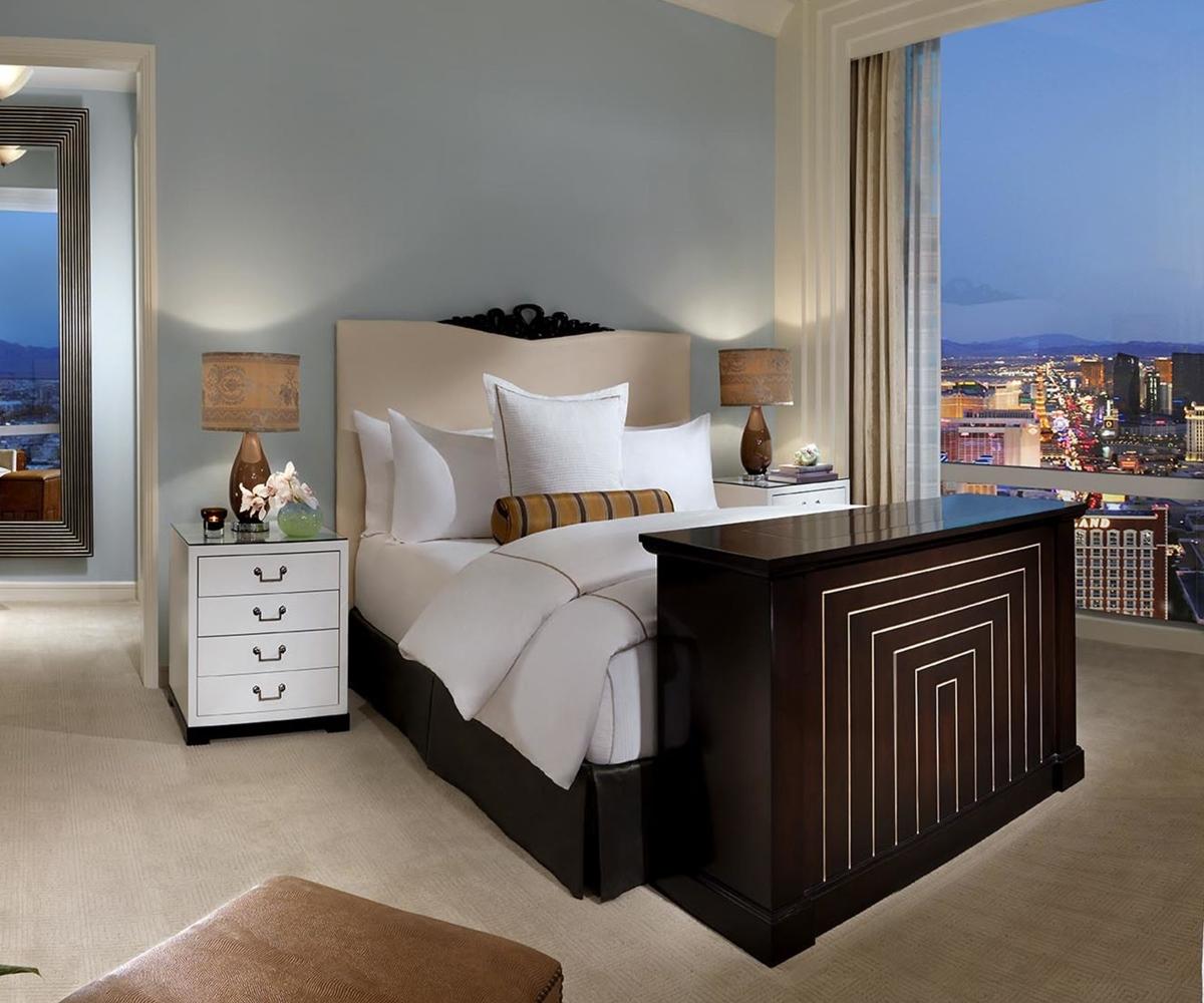 Trump International Hotel Лас Вегас Екстериор снимка The image shows a stylish hotel room featuring a comfortable bed with white and beige bedding. On either side of the bed are contemporary bedside tables with lamps. A unique piece of furniture resembling a desk or countertop is positioned at the foot