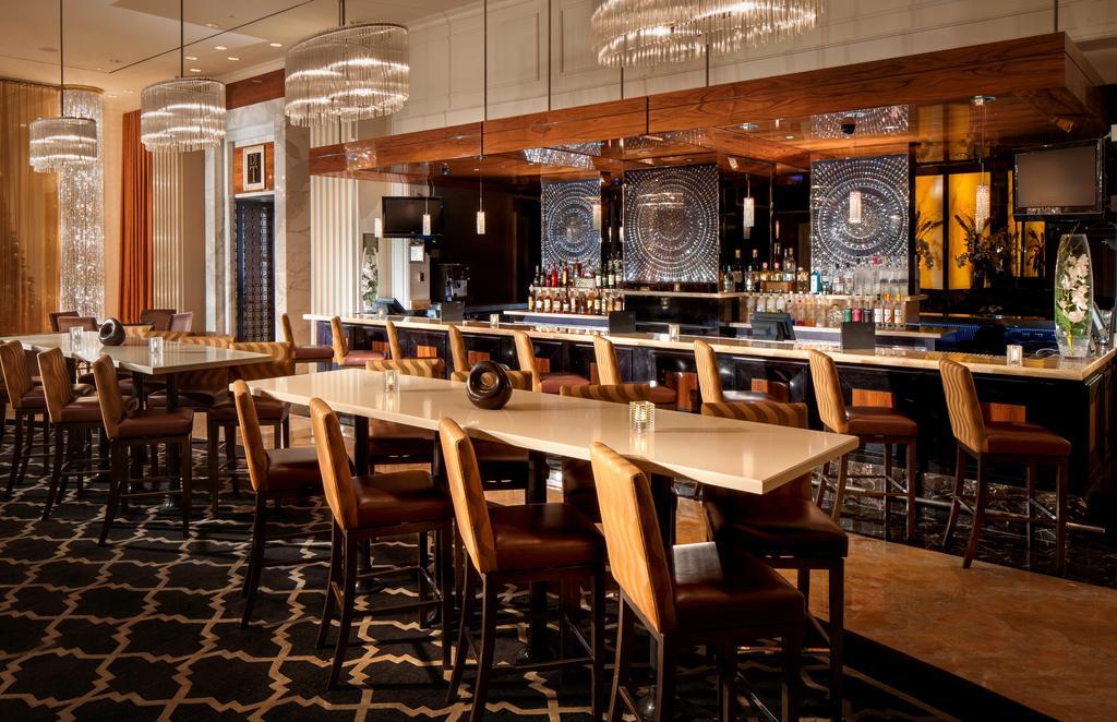 Trump International Hotel Лас Вегас Екстериор снимка The image shows a stylish restaurant or bar interior. There is a long, polished table positioned in front, with several high-back chairs around it. The bar area is in the background, featuring an extensive selection of bottles displayed on shelves an