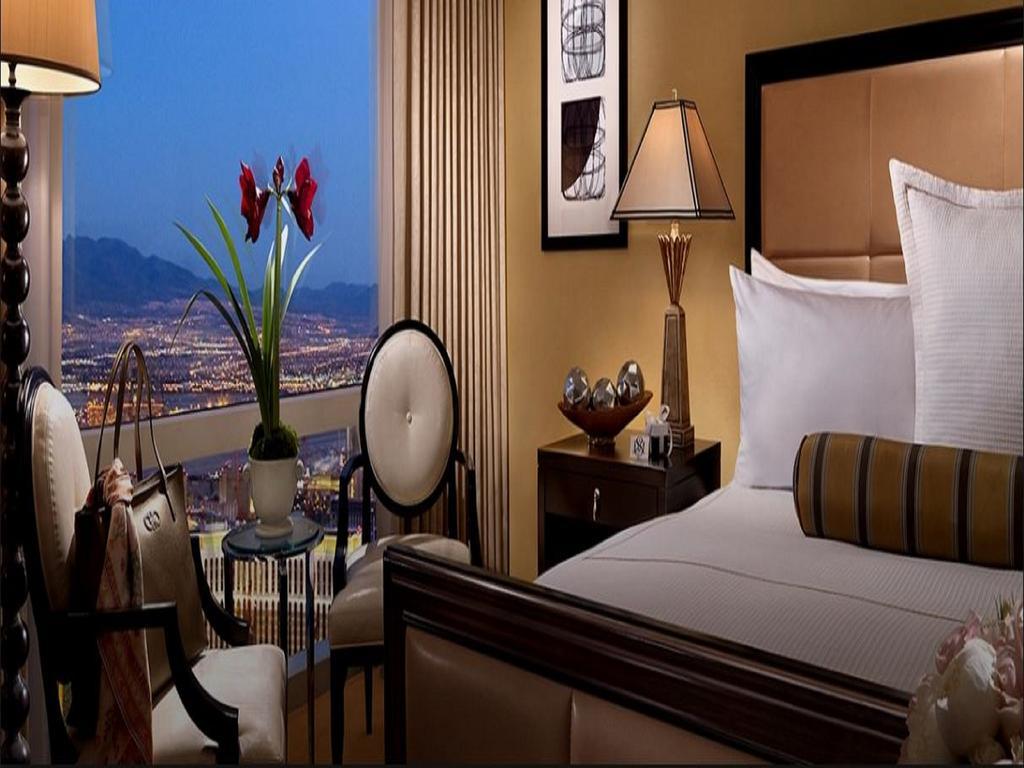 Trump International Hotel Лас Вегас Екстериор снимка The photo shows a luxurious hotel room with an elegant design. There is a large bed with crisp white linens and decorative pillows. To the side, there are two stylish chairs with a small table between them. A lamp provides soft lighting, and a decora