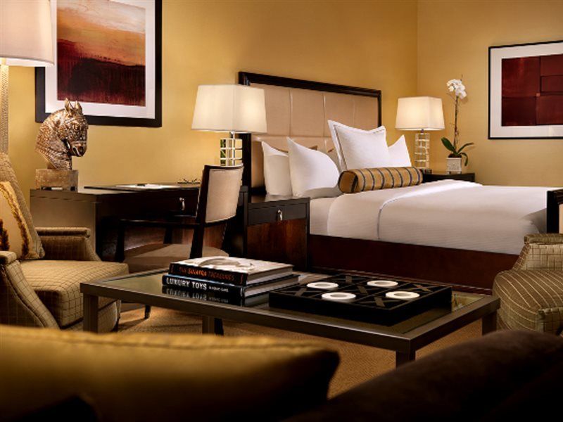 Trump International Hotel Лас Вегас Екстериор снимка The photo shows an elegantly furnished hotel room. It features a large bed with crisp white linens and decorative pillows. There are two bedside tables with lamps on either side of the bed, creating a warm ambiance. A small seating area is visible wi