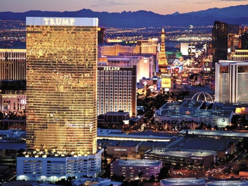 Trump International Hotel Лас Вегас Екстериор снимка The image shows a tall, gleaming building with a reflective gold facade, prominently bearing the name "Trump" at the top. The building is situated in Las Vegas, indicated by the surrounding bright city lights and recognizable landmarks in the backgro