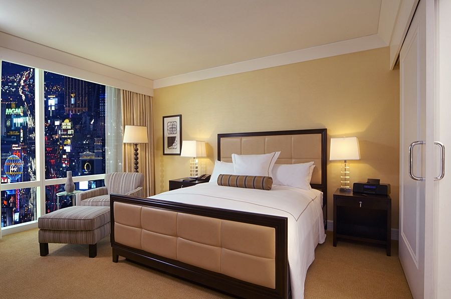 Trump International Hotel Лас Вегас Екстериор снимка The photo shows a stylish hotel room featuring a large bed with a padded headboard, adorned with white linens and a decorative throw. To the side of the bed, there is a small nightstand with a lamp. A cozy armchair is positioned nearby, along with a 