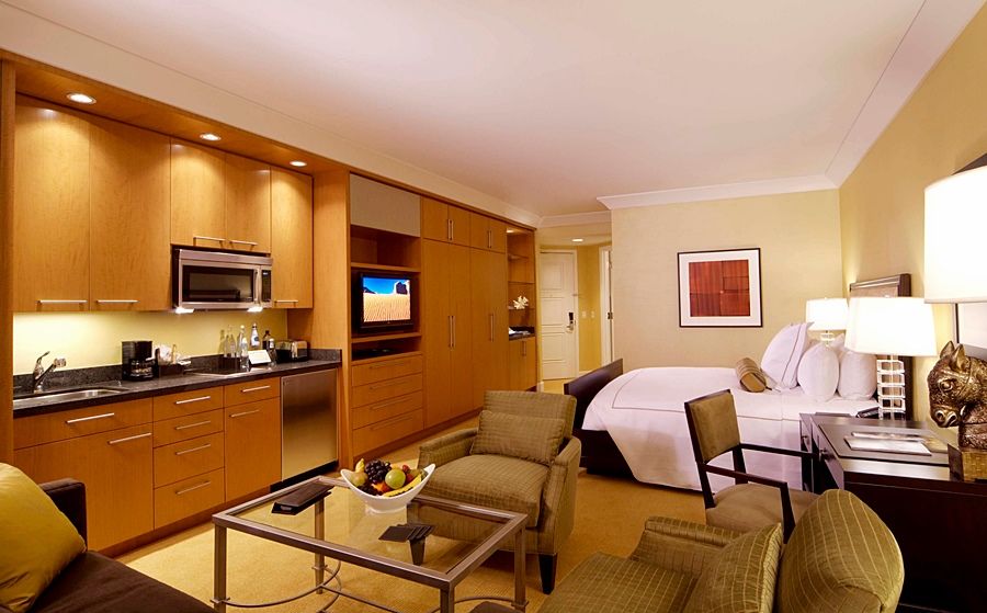 Trump International Hotel Лас Вегас Стая снимка The photo shows a modern hotel room or suite. It features a kitchenette on one side with wooden cabinetry, a microwave, and a small refrigerator. Opposite the kitchenette is a living area that includes a small dining table and chairs, as well as a co