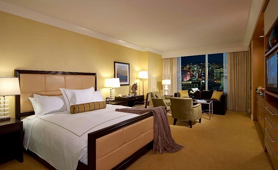 Trump International Hotel Лас Вегас Стая снимка The photo shows a luxurious hotel room featuring a large bed with plush bedding and a decorative throw. There are two armchairs and a small table in a cozy seating area, creating a welcoming atmosphere. The walls are painted in a warm yellow hue, and