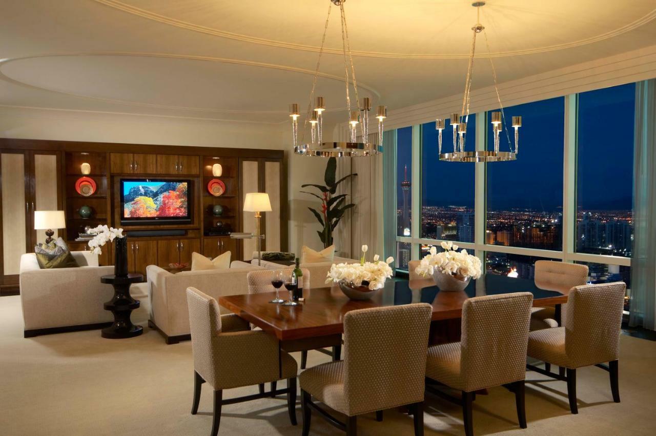 Trump International Hotel Лас Вегас Стая снимка The photo shows an elegantly designed living and dining area. The space features a large oval dining table surrounded by upholstered chairs. A decorative centerpiece with flowers adorns the table. On one side, there's a cozy seating arrangement with 