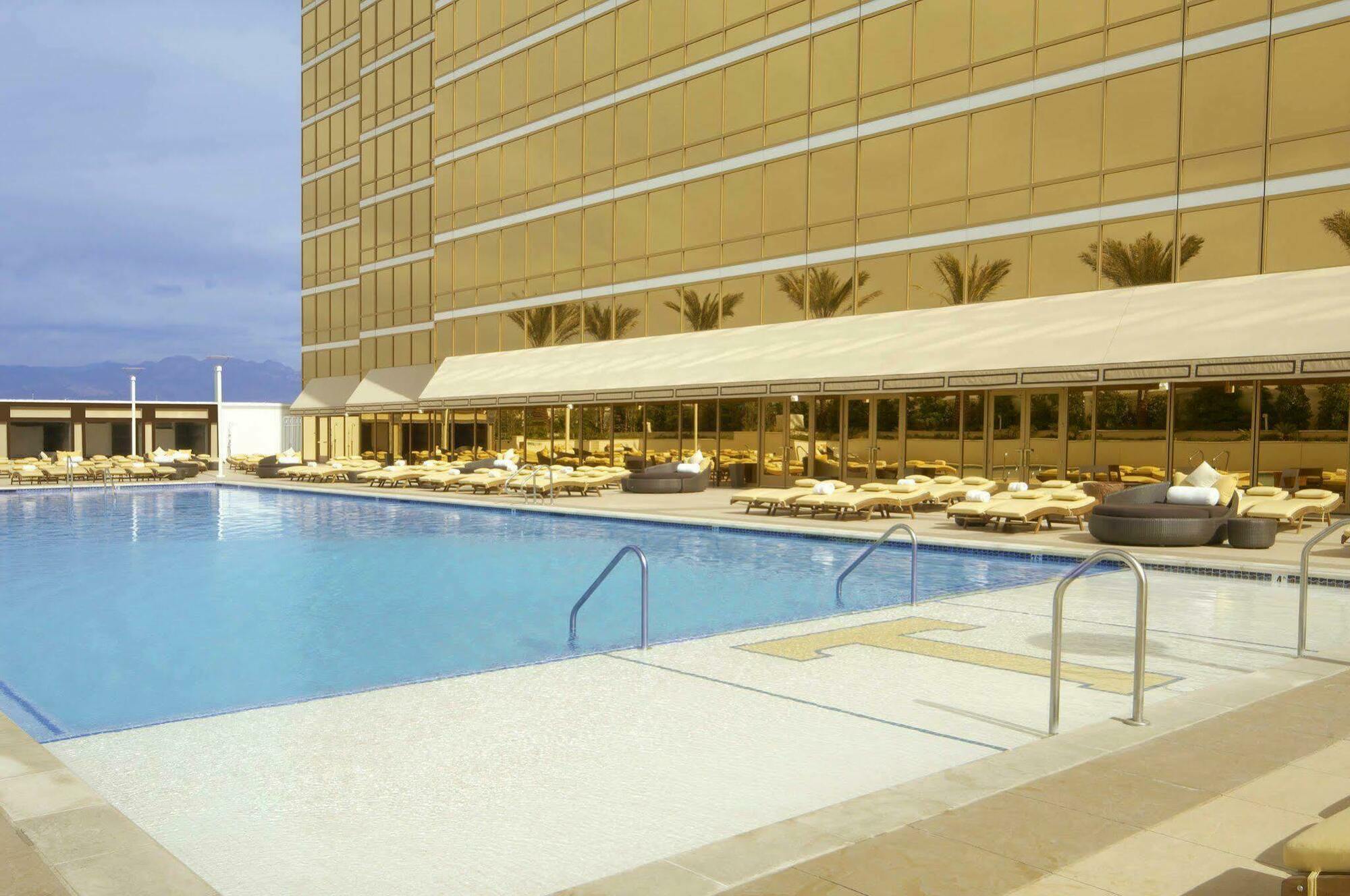 Trump International Hotel Лас Вегас Съоръжения снимка The photo shows a hotel pool area. There is a clear blue swimming pool with a set of stairs leading into it. Surrounding the pool are lounge chairs arranged for relaxation, and a shaded area with a structure likely serving as a dining or lounging spa
