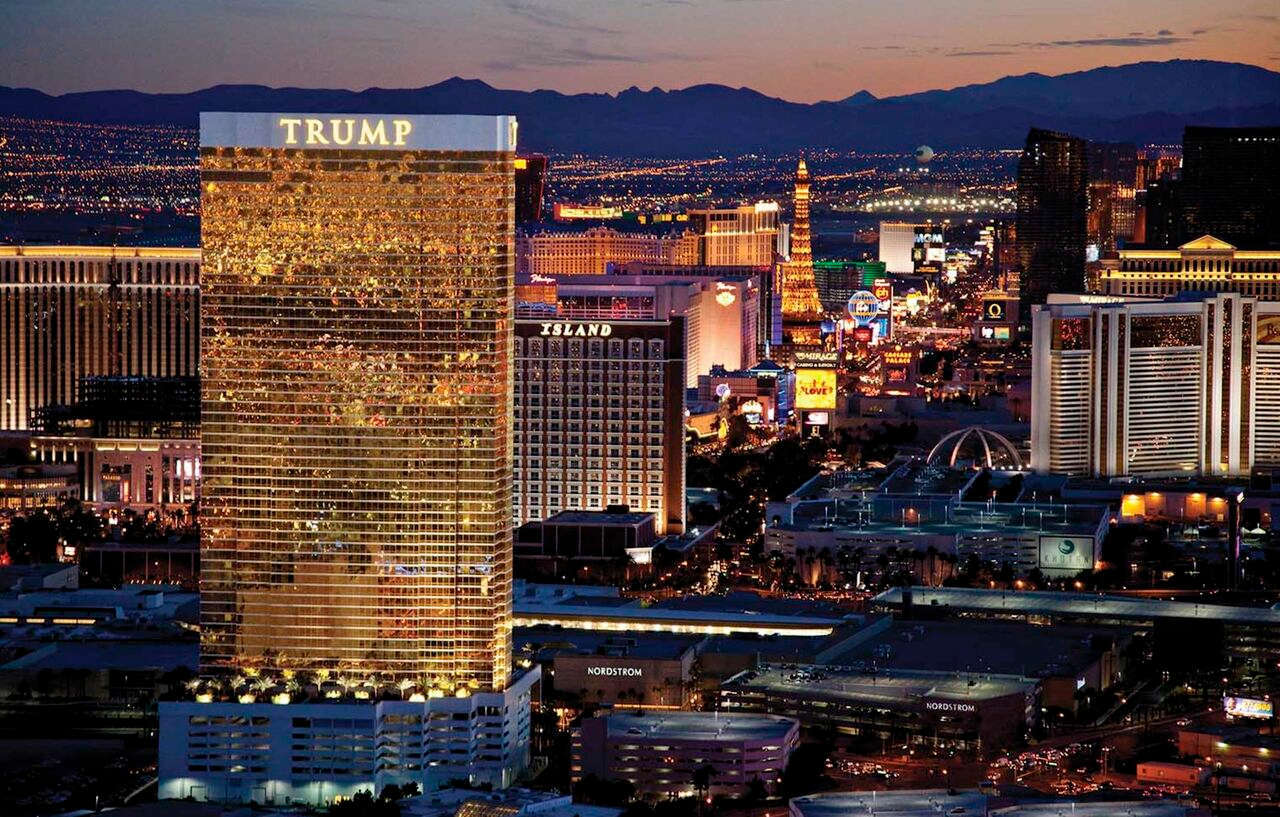 Trump International Hotel Лас Вегас Екстериор снимка The photo depicts the Trump International Hotel in Las Vegas, illuminated at dusk. The hotel is a tall building with a gold-tinted facade, reflecting the surrounding lights of the Las Vegas Strip. In the background, various other hotels and attractio