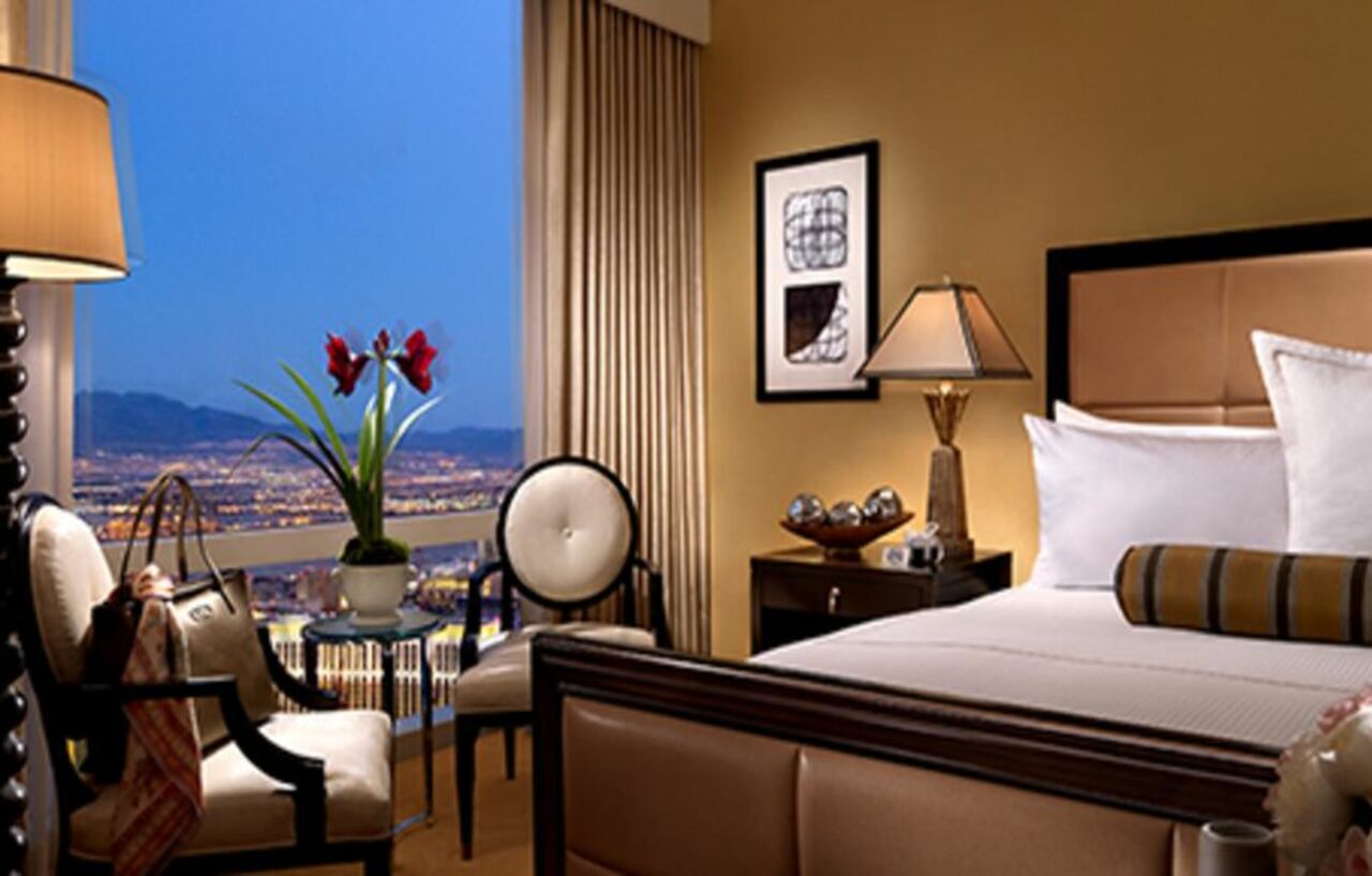 Trump International Hotel Лас Вегас Екстериор снимка The photo depicts a stylish hotel room with a luxurious ambiance. Features include a large bed with elegant bedding, a nightstand with a lamp, and a comfortable armchair paired with a small table. A decorative plant with red flowers adds a touch of c