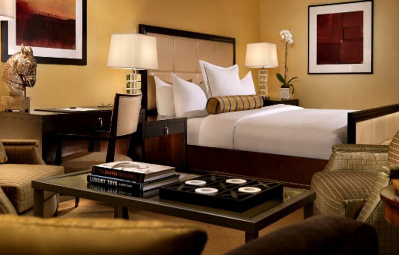 Trump International Hotel Лас Вегас Екстериор снимка The photo shows a stylish hotel room featuring a neatly made bed with white linens and decorative pillows. There are two bedside lamps on either side of the bed, providing soft lighting. In the foreground, a coffee table is set with decorative items,