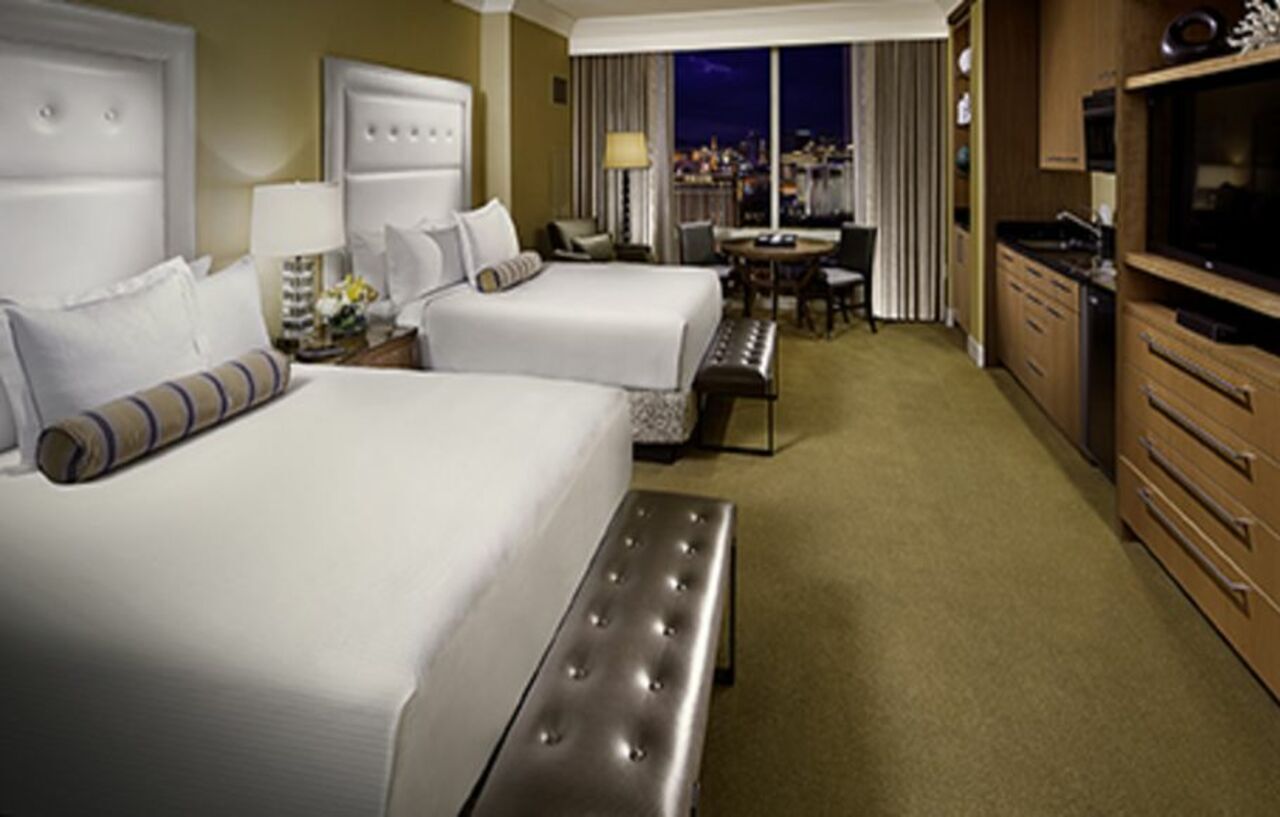 Trump International Hotel Лас Вегас Екстериор снимка The image shows a hotel room featuring two large beds with white bedding and decorative pillows. There's a stylish bench at the foot of each bed. The room is well-lit, with a window that offers a view of the city outside. A small dining table with ch