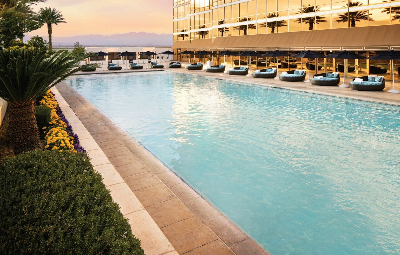 Trump International Hotel Лас Вегас Екстериор снимка The photo depicts a serene outdoor swimming pool area. The pool is large, featuring clear blue water, and is lined with a paved deck. On one side, there are lounge chairs with cushions, arranged neatly for relaxation. Surrounding the pool, you can se